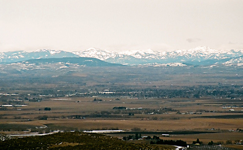 [Looking across fields with scattered buildings and snow-capped mountains as a backdrop.]